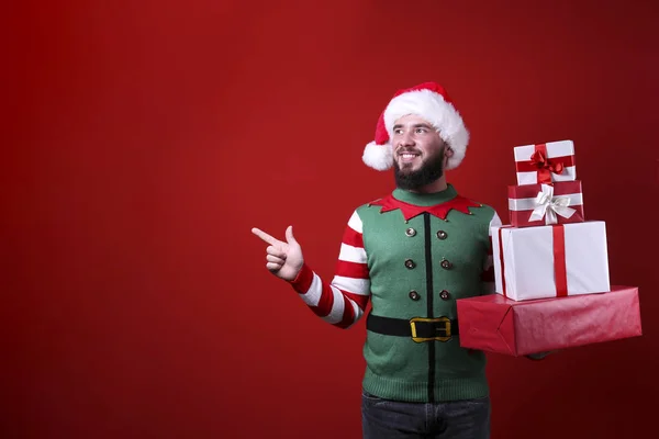 Jongeman met perfect geprepareerde baard in kerstoutfit op rode muurachtergrond. — Stockfoto