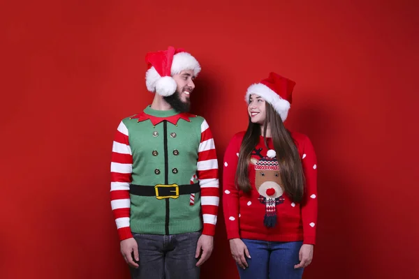 Smiling young couple wearing santa hats on red wall background. — Stock Photo, Image