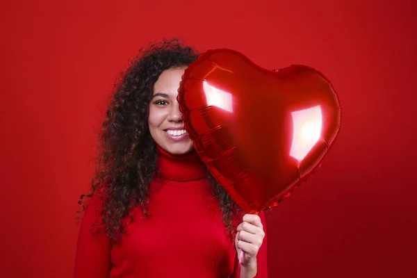 Preciosa joven posando sobre pared roja sosteniendo helio inflado globo . — Foto de Stock