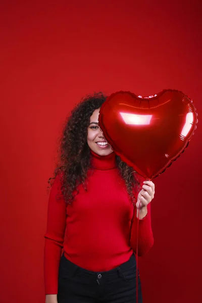 Preciosa joven posando sobre pared roja sosteniendo helio inflado globo . — Foto de Stock