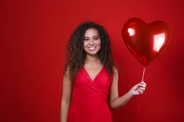 Preciosa joven posando sobre pared roja sosteniendo helio inflado globo . — Foto de Stock