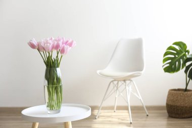 Glass vase with spring flowers on small white coffee table.