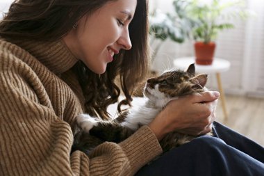 Charismatic young woman playing with her adorable cat. clipart