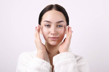 Young female wearing white robe and applying cosmetics on her face.