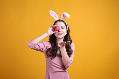 Paskalya için geleneksel tavşan kulaklığı takan ve gülümseyen genç bir kadının stüdyo portresi. Sarı arka planda dalgalı saçlı esmer kadın. Kapat, boşluğu kopyala.