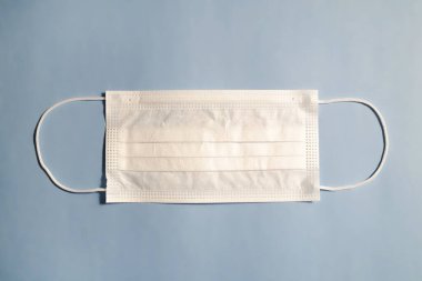 Tek kullanımlık yüz maskesi mavi desenli masa arkaplanı üzerinde. Virüs yaymak için koruyucu raspiratuar maskesi. Kapat, boşluğu kopyala, üst görünüm, düz yatış.