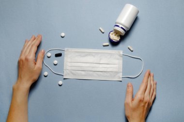 First person view of woman's hands on blue table with face mask, preventing drugs & vitamins. Protective raspiratory mask for spreading virus. Close up, copy space, top view, flat lay, background.