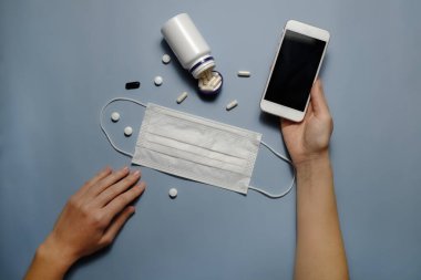 Checking news on coronavirus concept. Blue table with face mask, preventing drugs & vitamins. Protective raspiratory mask for spreading virus. Close up, copy space, top view, flat lay, background.