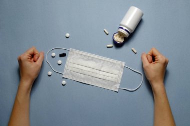 First person view of woman's hands on blue table with face mask, preventing drugs & vitamins. Protective raspiratory mask for spreading virus. Close up, copy space, top view, flat lay, background.