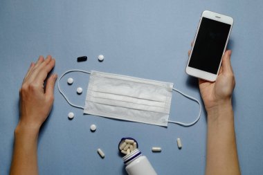 Checking news on coronavirus concept. Blue table with face mask, preventing drugs & vitamins. Protective raspiratory mask for spreading virus. Close up, copy space, top view, flat lay, background.