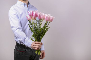 Pamuk gömlek giyen, elinde güzel bir buket pembe çiçek tutan genç adamın stüdyo fotoğrafı. Kapat, kopyala boşluk, arkaplan.