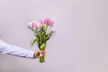 Pamuk gömlek giyen, elinde güzel bir buket pembe çiçek tutan genç adamın stüdyo fotoğrafı. Kapat, kopyala boşluk, arkaplan.