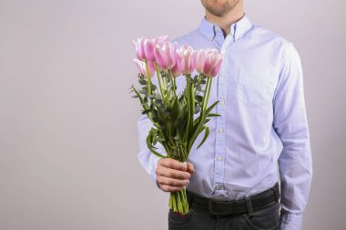 Pamuk gömlek giyen, elinde güzel bir buket pembe çiçek tutan genç adamın stüdyo fotoğrafı. Kapat, kopyala boşluk, arkaplan.