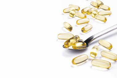 Omega 3 balık karaciğer yağı kapsülleri kaşık içinde. Tecrit edilmiş arka planda büyük altın saydam haplar. Her gün sağlıklı yağ asitleri besin takviyesi. Üst görünüm, düz görünüm, kopyalama alanı, kapat