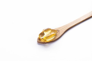 Tahta kaşıkta omega 3 balık ciğeri yağı kapsülleri. Tecrit edilmiş arka planda büyük altın saydam haplar. Sağlıklı günlük yağ asitleri besin takviyesi. Üst görünüm, düz görünüm, kopyalama alanı, kapat