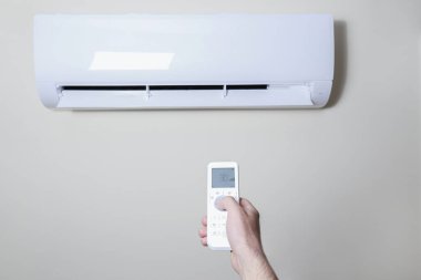 Yeni kurulmuş beyaz klimanın uzaktan kumandasını tutarken yakın çekim. Pastel renkli duvarda asılı duran klima çalışıyor ve metin için bir sürü kopya alanı var. Arkaplan.