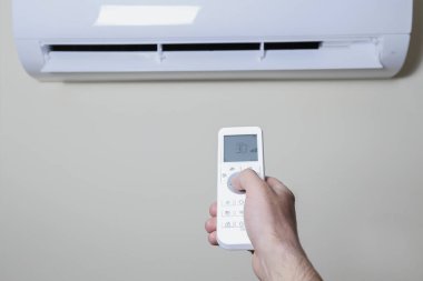 Yeni kurulmuş beyaz klimanın uzaktan kumandasını tutarken yakın çekim. Pastel renkli duvarda asılı duran klima çalışıyor ve metin için bir sürü kopya alanı var. Arkaplan.