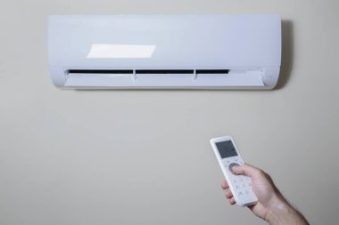 Yeni kurulmuş beyaz klimanın uzaktan kumandasını tutarken yakın çekim. Pastel renkli duvarda asılı duran klima çalışıyor ve metin için bir sürü kopya alanı var. Arkaplan.