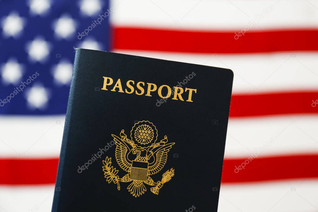 Latest version of United States of America citizen Passport with biometric ID chip standing on table with USA flag on background. Person identification document. Close up, copy space.