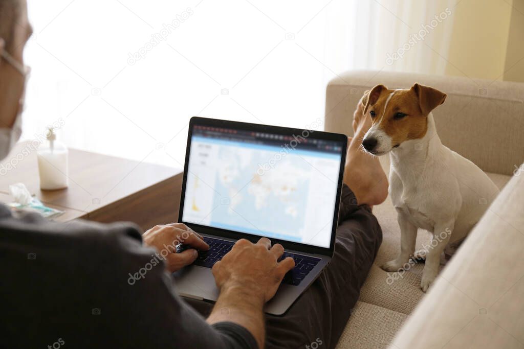 Close up shot of adult man working at home due to coronavirus quarantine concept. Male sitting on couch with his dog and laptop. Jack russell terrier puppy with owner. Background, copy space.