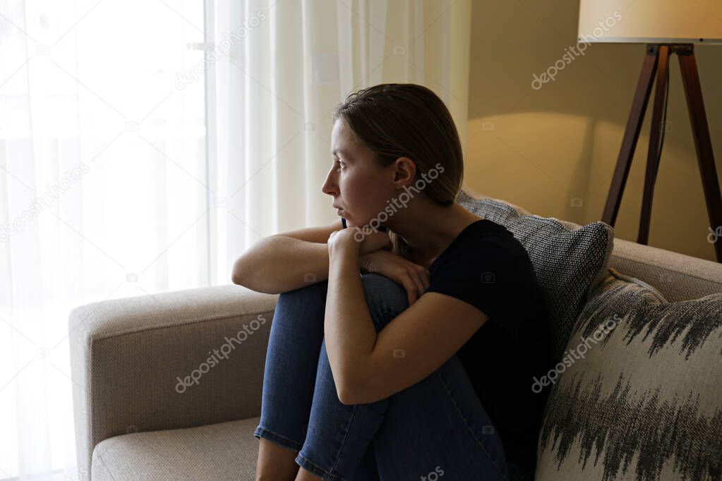 Depressed single woman sitting at home due to worldwide quarantine lockdown. Portrait of lonely stressed out female alone in her bed. Close up, copy space, background.