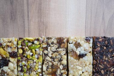 Karışık glütensiz tahıl gevreği enerji barları, kurutulmuş meyve, şam fıstığı ve ahşap arka planda çeşitli fındıklar. Sağlıklı vejetaryen süper yiyecekler, spor yaşam tarzı için diyet aperatifleri. Üst görünüm, alanı kopyala