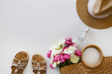 Kadınların bahar çiçekleriyle süslü hasır çantasının kavramsal görüntüsü. Beyaz arka planda renkli beyaz ve pembe ranunculus buketi. Kapat, kopyala boşluk, kırpılmış çekim.