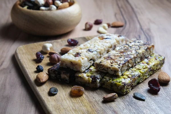 Mixed gluten free granola cereal energy bars with dried fruit, pistachio & various nuts on wooden background. Healthy vegan super food, fitness dieting snack for sporty lifestyle. Top view, copy space