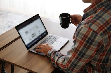 Kanepede oturan, dizüstü bilgisayar kullanan, internette gezinen, sıcak içecek içen tanınmamış bir adamın görüntüsü. Kendini soyutlama dönemi konsepti boyunca evden çalışmak. Kapat, kopyala boşluk, arkaplan.