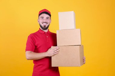 Kırmızı üniformalı ve şapkalı genç teslimatçı, boş karton kutuyu izole edilmiş beyaz arka planda tutuyor. Paket taşıyan dost canlısı sakallı adamın portresi. Metin için alanı kopyala.