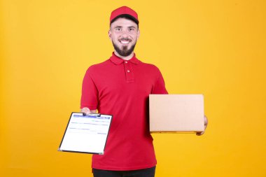 Kırmızı üniformalı ve şapkalı genç teslimatçı, boş karton kutuyu izole edilmiş beyaz arka planda tutuyor. Paket taşıyan dost canlısı sakallı adamın portresi. Metin için alanı kopyala.