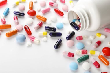 Patlamış plastik şişeden masaya saçılmış farklı renkli haplarla bezenmiş düz bir kompozisyon. Açılmış ilaç yığınları beyaz kağıtlı arka planda. Kapat, metin için boşluk kopyala