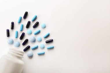 Patlamış plastik şişeden masaya saçılmış farklı renkli haplarla bezenmiş düz bir kompozisyon. Açılmış ilaç yığınları beyaz kağıtlı arka planda. Kapat, metin için boşluk kopyala