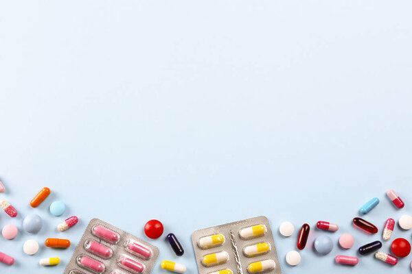 Flat lay composition with bunch of different colorful pills scattered over the table. Pile of opened medication on blue paper textured background. Close up, copy space for text.