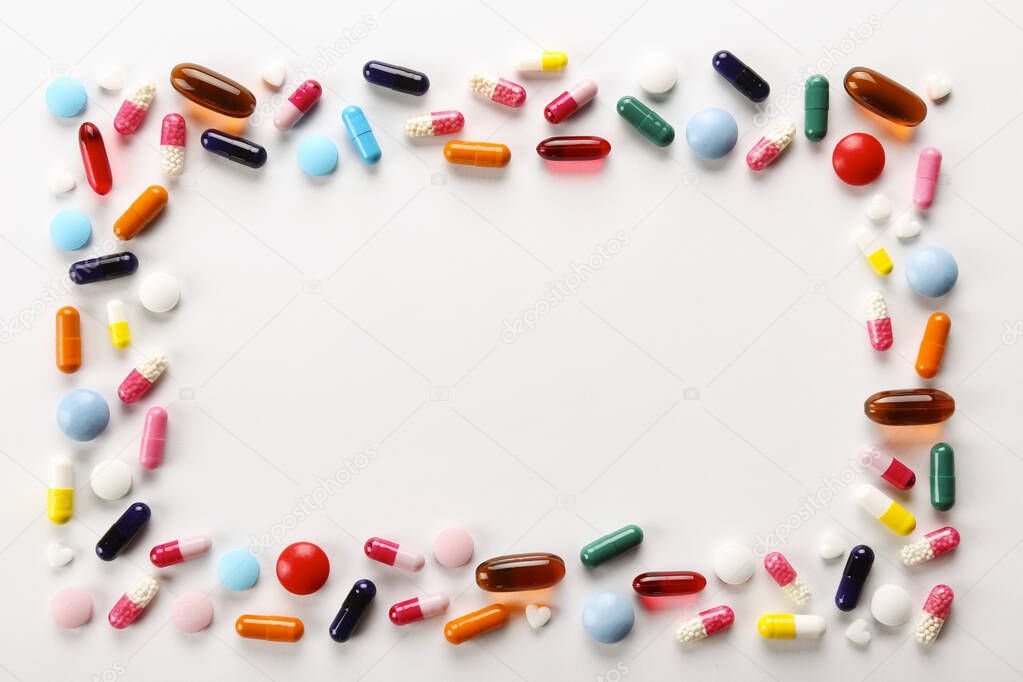 Flat lay composition with bunch of different colorful pills scattered over the table. Pile of opened medication on white paper textured background. Close up, copy space for text.