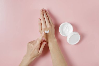 Aşırı sabun ve dezenfektan kullandıktan sonra iyileşme ve iyileşme için el kreminin canlandırılması. Genç bir kadın nemlendirici losyon sürüyor. Boşluğu kopyala, kapat, pembe arkaplan, düz alan, üst görünüm.