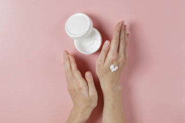 Aşırı sabun ve dezenfektan kullandıktan sonra iyileşme ve iyileşme için el kreminin canlandırılması. Genç bir kadın nemlendirici losyon sürüyor. Boşluğu kopyala, kapat, pembe arkaplan, düz alan, üst görünüm.