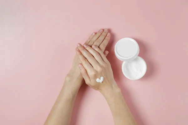 Revitalizing hand cream for healing and recovery after excessive use of soap and disinfectants. Young woman applying moisturizing lotion. Copy space, close up, pink background, flat lay, top view.