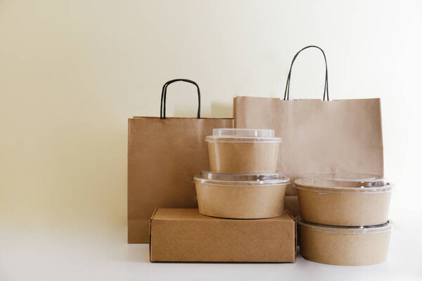 Bunch of blank disposable containers for takeout food stacked with paper bags and boxes with copy space for brand's logo. Close up shot of eco friendly to go carton bowls on table.