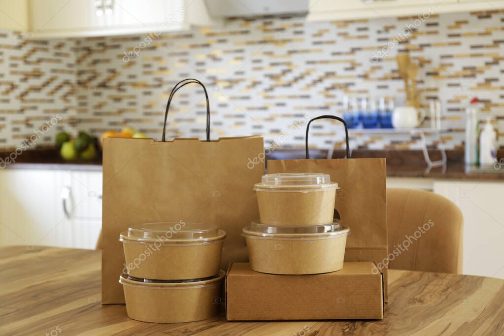 Bunch of blank disposable containers for takeout food stacked with paper bags and boxes with copy space for brand's logo. Close up shot of eco friendly to go carton bowls on table.