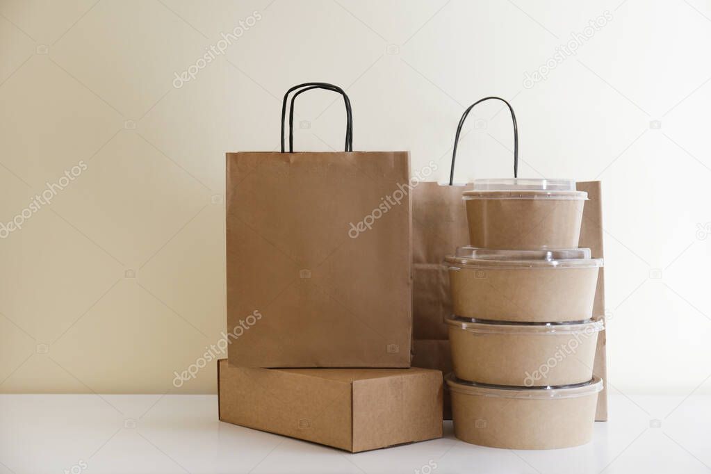 Bunch of blank disposable containers for takeout food stacked with paper bags and boxes with copy space for brand's logo. Close up shot of eco friendly to go carton bowls on table.