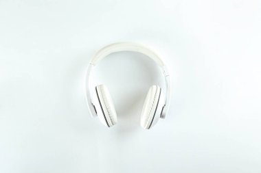Minimalist üst görünüm kompozisyonu, beyaz kulaklıklar ve parlak kağıt kaplamalı arka plan. Metnin için bir sürü kopya alanı var. Yaklaş, düz yat..