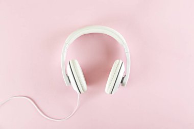 Minimalist üst görünüm kompozisyonu, beyaz kulaklıklar ve parlak kağıt kaplamalı arka plan. Metnin için bir sürü kopya alanı var. Yaklaş, düz yat..