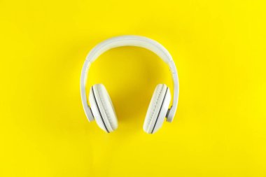 Minimalist üst görünüm kompozisyonu, beyaz kulaklıklar ve parlak kağıt kaplamalı arka plan. Metnin için bir sürü kopya alanı var. Yaklaş, düz yat..