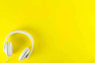 Minimalist üst görünüm kompozisyonu, beyaz kulaklıklar ve parlak kağıt kaplamalı arka plan. Metnin için bir sürü kopya alanı var. Yaklaş, düz yat..