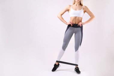 Tanımlanamayan formda, boş kolsuz bluz ve yoga pantolonu giyen, spor bandıyla egzersiz yapan bir kadının yakın çekimi. Beyaz arka planda izole edilmiş. Spor giyim sektöründe çekici bir kadın. Metin için alanı kopyala.