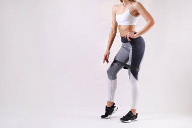 Tanımlanamayan formda, boş kolsuz bluz ve yoga pantolonu giyen, spor bandıyla egzersiz yapan bir kadının yakın çekimi. Beyaz arka planda izole edilmiş. Spor giyim sektöründe çekici bir kadın. Metin için alanı kopyala.