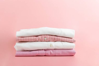 Renkli, mükemmel katlanmış giysi yığını. Farklı renkte gömlek ve süveter yığınları soluk pembe arka planda izole edilmiş. Kapat, üst görünüm, boşluğu kopyala.