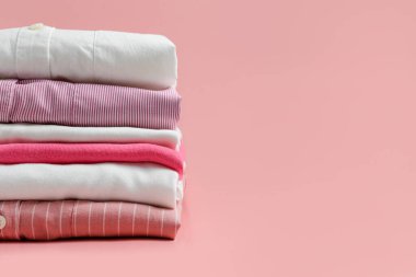 Renkli, mükemmel katlanmış giysi yığını. Farklı renkte gömlek ve süveter yığınları soluk pembe arka planda izole edilmiş. Kapat, boşluğu kopyala.