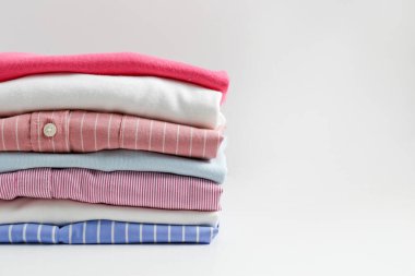 Renkli, mükemmel katlanmış giysi yığını. Farklı pastel renkli gömlek yığınları, izole edilmiş süveterler ve beyaz arka planda başka giysiler. Kapat, boşluğu kopyala.